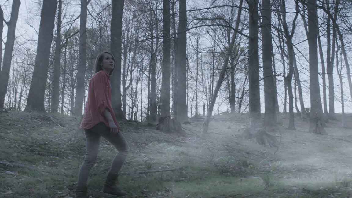 Woman walking through dense fog in a creepy forest